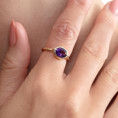 a woman's hand wearing a gold ring with an oval amethyst stone