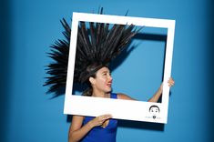 a woman holding up a framed photo with black feathers on her head and an emoticive expression