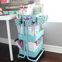 a cart filled with lots of office supplies on top of a hard wood floor next to a white table