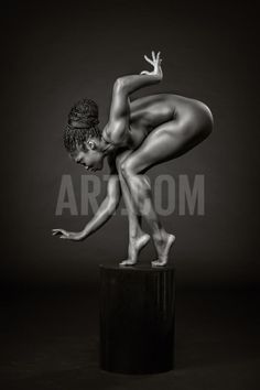 a black and white photo of a naked woman leaning on a pedestal with her hands in the air