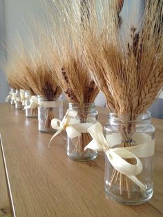 three glass jars filled with dried wheat on top of a wooden table