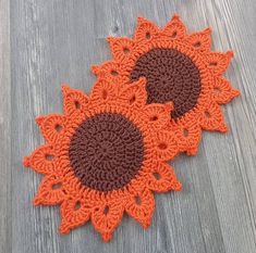 three crocheted sunflowers on a wooden floor with one orange and the other brown