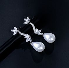 Romantic and elegant, this exquisite pair of earrings features iridescent white pearls and clear cubic zirconia that capture the light from every angle with a perfectly translucent appeal. The earrings are rhodium plated for a bright finish which enhances the intricate detailing and conveys a modern take on old elegance. Overall length of the earring is 38mm (approx. 1.5"). This exquisite design will add a touch of sophistication to any wedding gown or formal ensemble. Cubic Zirconia Bridal Earrings, Iridescent White, Bridal Earrings, Exquisite Design, Wedding Gown, Pearl White, Rhodium Plated, Wedding Gowns, Diamond Earrings