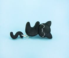 a black cat keychain is laying down on a blue surface with its eyes closed