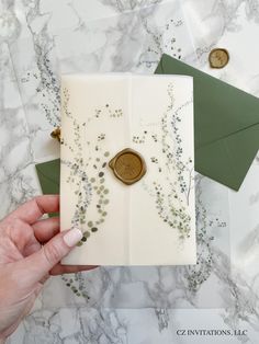 a hand holding an envelope with a wax stamp on it and some green envelopes next to it