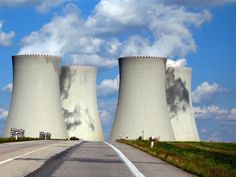 two large cooling towers sitting next to each other on a road under a cloudy blue sky