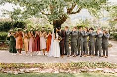 a group of people standing next to each other in front of a tree with their hands up