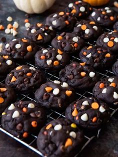 chocolate cookies with sprinkles and candy on a cooling rack next to an orange pumpkin