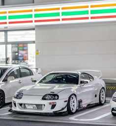 three cars are parked in a parking lot with gas prices on the wall behind them