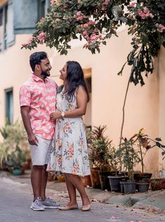 a man and woman standing next to each other in front of a tree with pink flowers