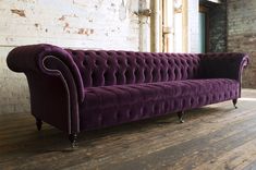 a purple couch sitting on top of a wooden floor next to a brick wall in an old building