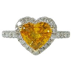 Prepare to be captivated by the exquisite IGI certified 18K white gold 1.29ct heart-shaped Yellow Sapphire (vivid orangy yellow) and 0.41ct diamond ring, a true masterpiece of fine jewelry design. At the center of this stunning ring is a magnificent 1.29 carat Yellow Sapphire, boasting a rare and mesmerizing vivid orangy-yellow hue. Expertly cut into a heart shape, this exceptional gemstone takes center stage, radiating a warm and vibrant glow that is simply breathtaking. Certified by the prestigious IGI (International Gemological Institute), this Yellow Sapphire is a true rarity, showcasing its natural and untreated beauty in a stunning heart shape that adds a touch of romance and elegance to the design. Surrounding the captivating Sapphire is a classic halo setting, featuring 32 round br Fine Jewelry Design, Vintage Cocktail Ring, Swirl Ring, Pink Sapphire Ring, Sapphire And Diamond Ring, Purple Sapphire, Halo Setting, Blue Sapphire Diamond, Sapphire Diamond Ring