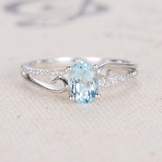 an oval aqua blue topazte and diamond ring on a white cloth with the word love written below it