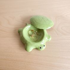 a green turtle shaped ring dish with two rings in it's shell on a wooden surface