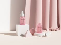 two bottles of skin care sitting next to each other on a white surface with pink curtains in the background