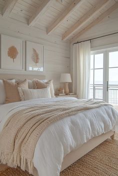 a large bed sitting in a bedroom next to a window with white sheets and pillows