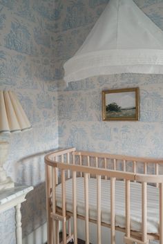 a baby's crib in a room with blue wallpaper and a painting on the wall