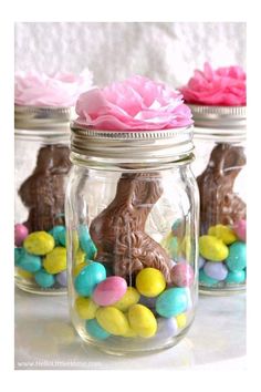 mason jar easter baskets filled with chocolate bunny eggs and pink flowers in the center, sitting on a white table