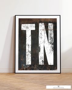 the letter n is displayed in front of a white wall with wood flooring and a black frame