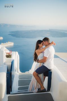 a man and woman kissing on top of a building with the ocean in the background