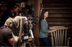 a woman standing in front of a wooden chair next to a camera man and another person