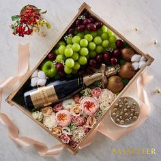 a wine bottle and some grapes in a box with pink ribbon on the floor next to it