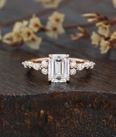 an emerald cut diamond ring on top of a wooden surface with flowers in the background