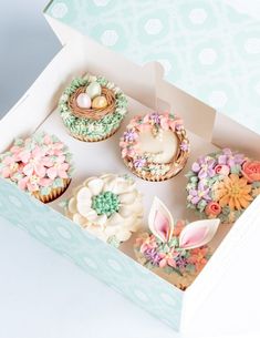 an open box filled with cupcakes covered in frosting and decorated with flowers