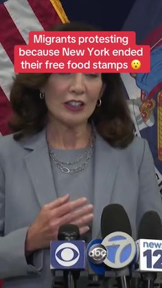 a woman standing in front of microphones with an american flag behind her