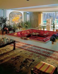 a living room filled with red couches and lots of plants on top of it