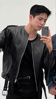 a young man wearing a black leather jacket and holding a cell phone in his hand