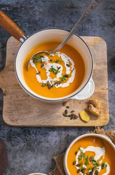 two bowls of carrot soup with sour cream and garnish on the top one has a spoon in it