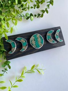 three green and silver crescent shaped brooches sitting on top of a wooden plaque