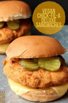 two chicken burgers with pickles and cheese on the bun, sitting next to each other