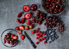 berries, strawberries, and blueberries are arranged on a table with a bowl of cherries