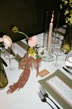 the table is set with wine glasses, silverware and flowers in vases on it