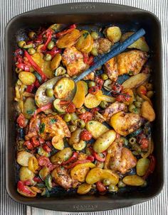 a pan filled with chicken and vegetables on top of a striped table cloth next to a spoon