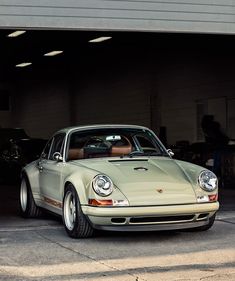 a green porsche parked in front of a garage