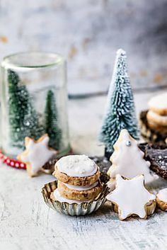 some cookies are sitting on a table next to christmas trees and glass jars with frosting