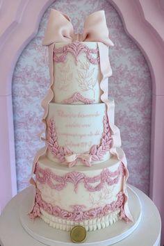 a three tiered cake with pink decorations and bows on top, sitting on a table in front of a purple wall