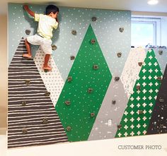 a young boy climbing up the side of a wall covered in colorful paper trees and polka dots