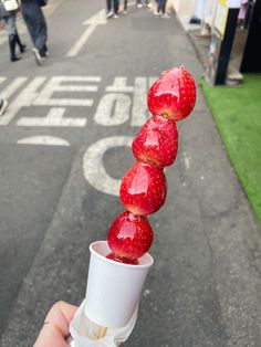 a person is holding up some strawberries on a stick in the middle of the street