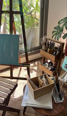 an easel sitting on top of a wooden floor next to a window filled with paint