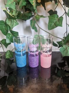 three different colored glasses sitting on top of a table next to a green leafy plant