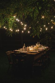 an outdoor dinner table is set with candles and wine bottles, surrounded by string lights