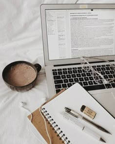 an open laptop computer sitting on top of a bed next to a cup of coffee