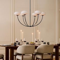 a chandelier hanging over a dining room table with wine glasses and candles on it