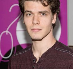 a young man is posing for the camera in front of a purple wall and logo