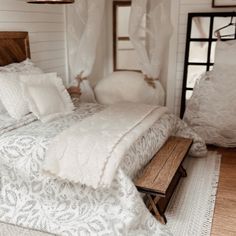 a bed with white sheets and pillows on top of it next to a wooden bench