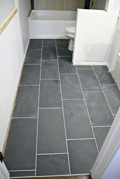 a bathroom with gray tile flooring next to a white toilet and bathtub in the corner